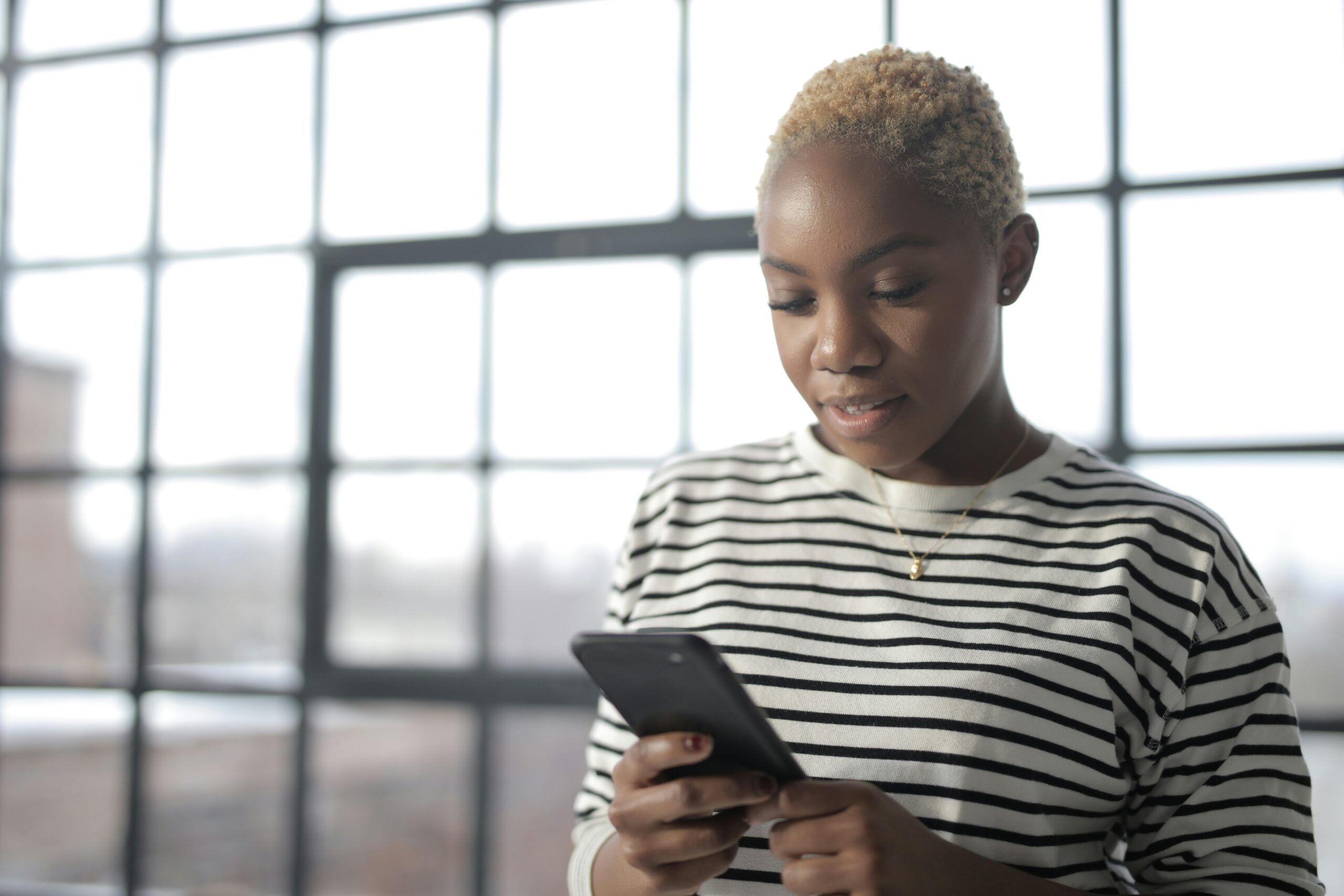 A Nigerian female student in white and black striped crew neck shirt holding black smartphone