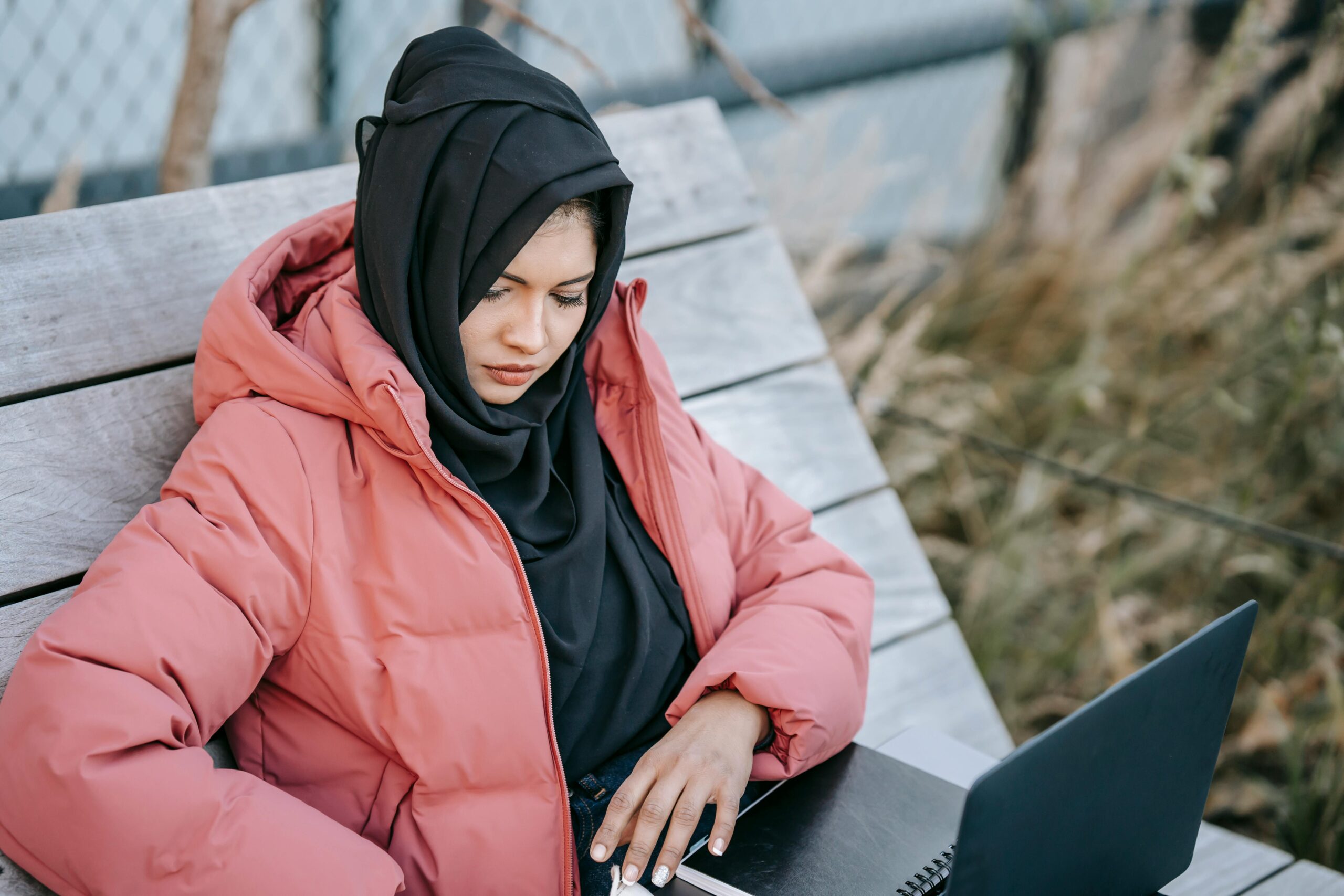 Female college student working on laptop with notebook in park