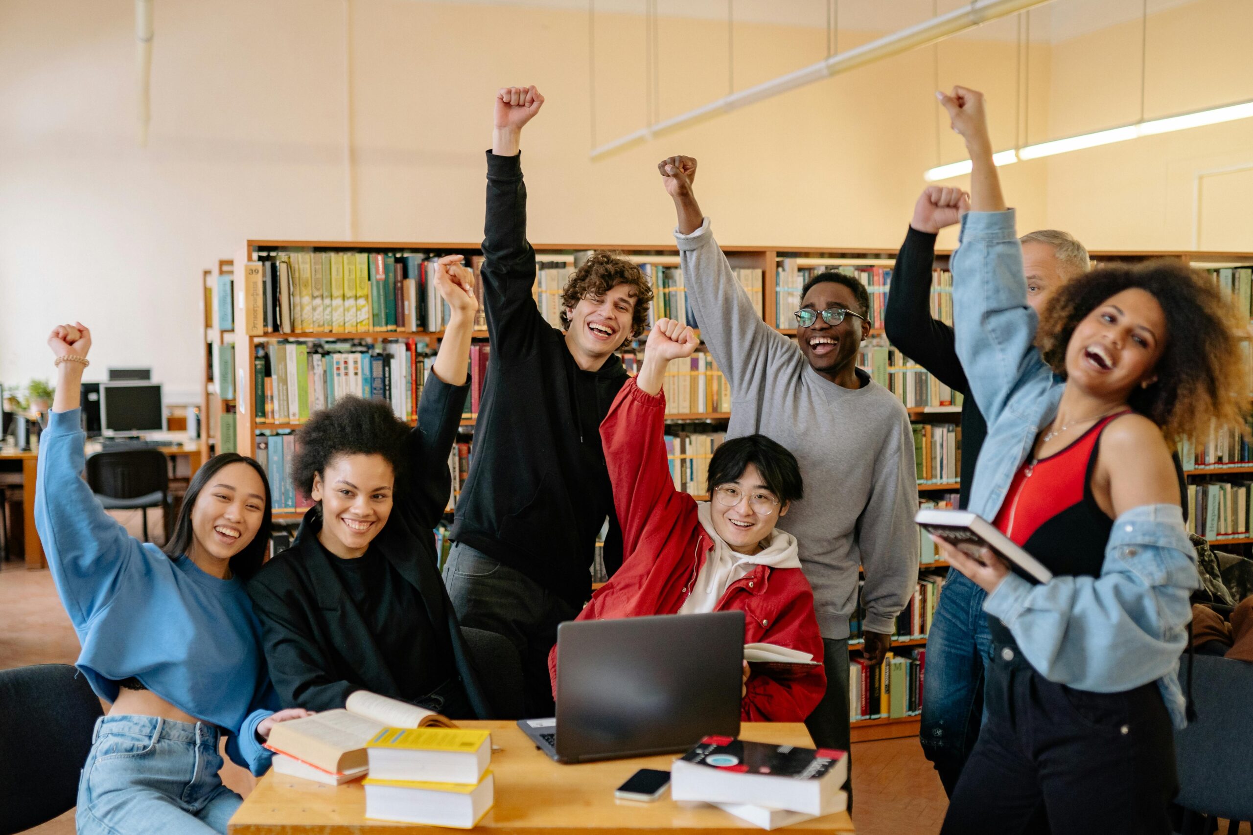 Group of student smiling and standing near brown wooden table raising hands