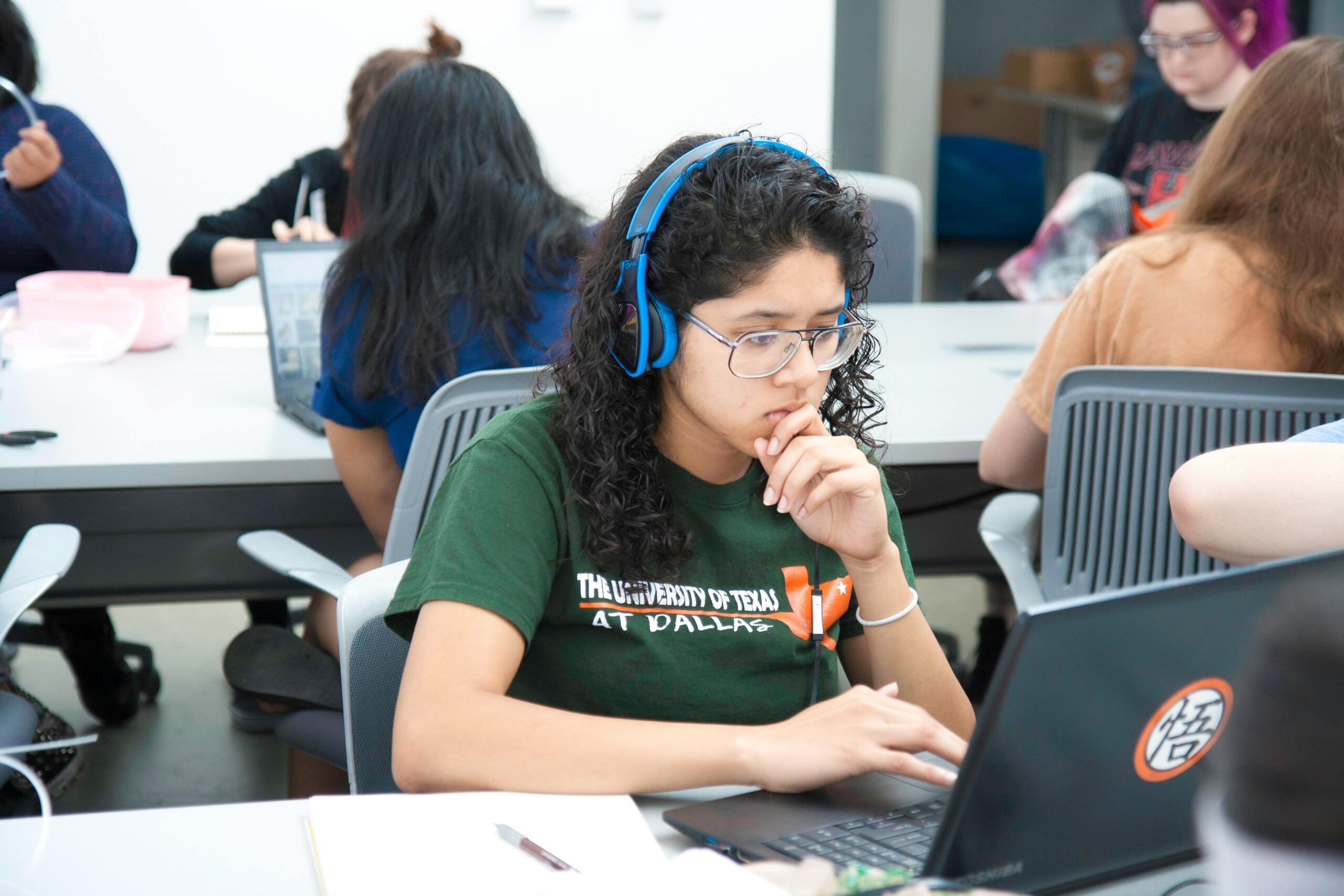 A female university student wearing blue headphones and studying on her Laptop