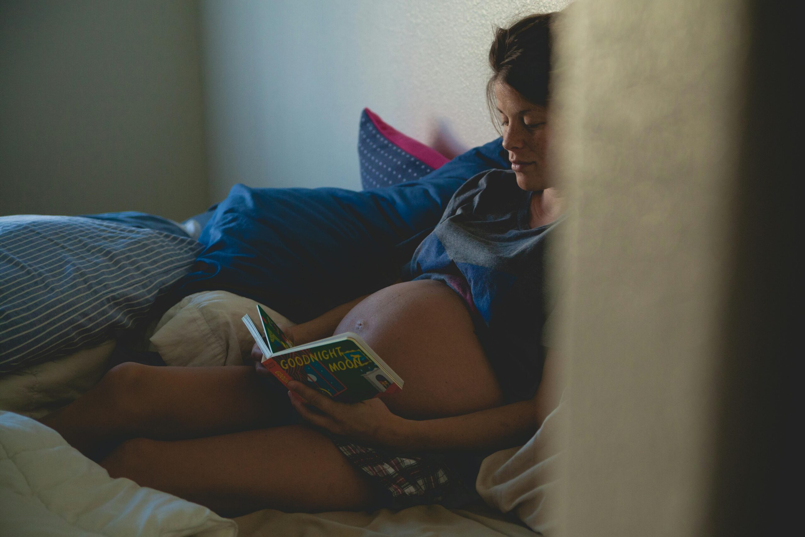 A pregnant student sitting on bed and reading book