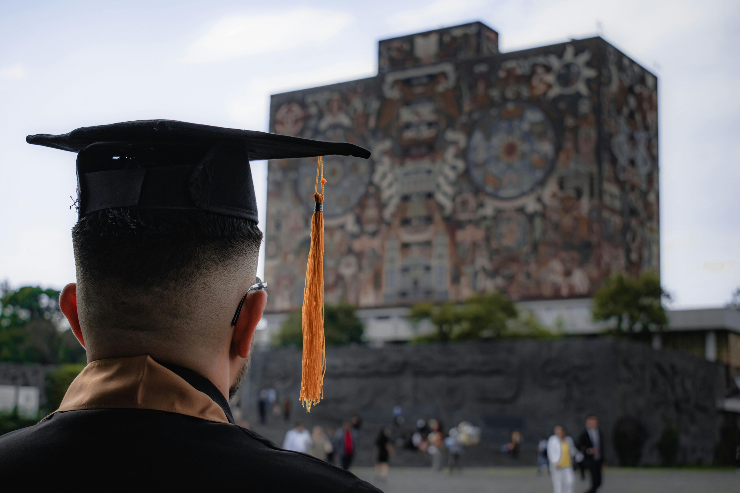 A male Alumni Wearing a Mortarboard Looking at the University Building