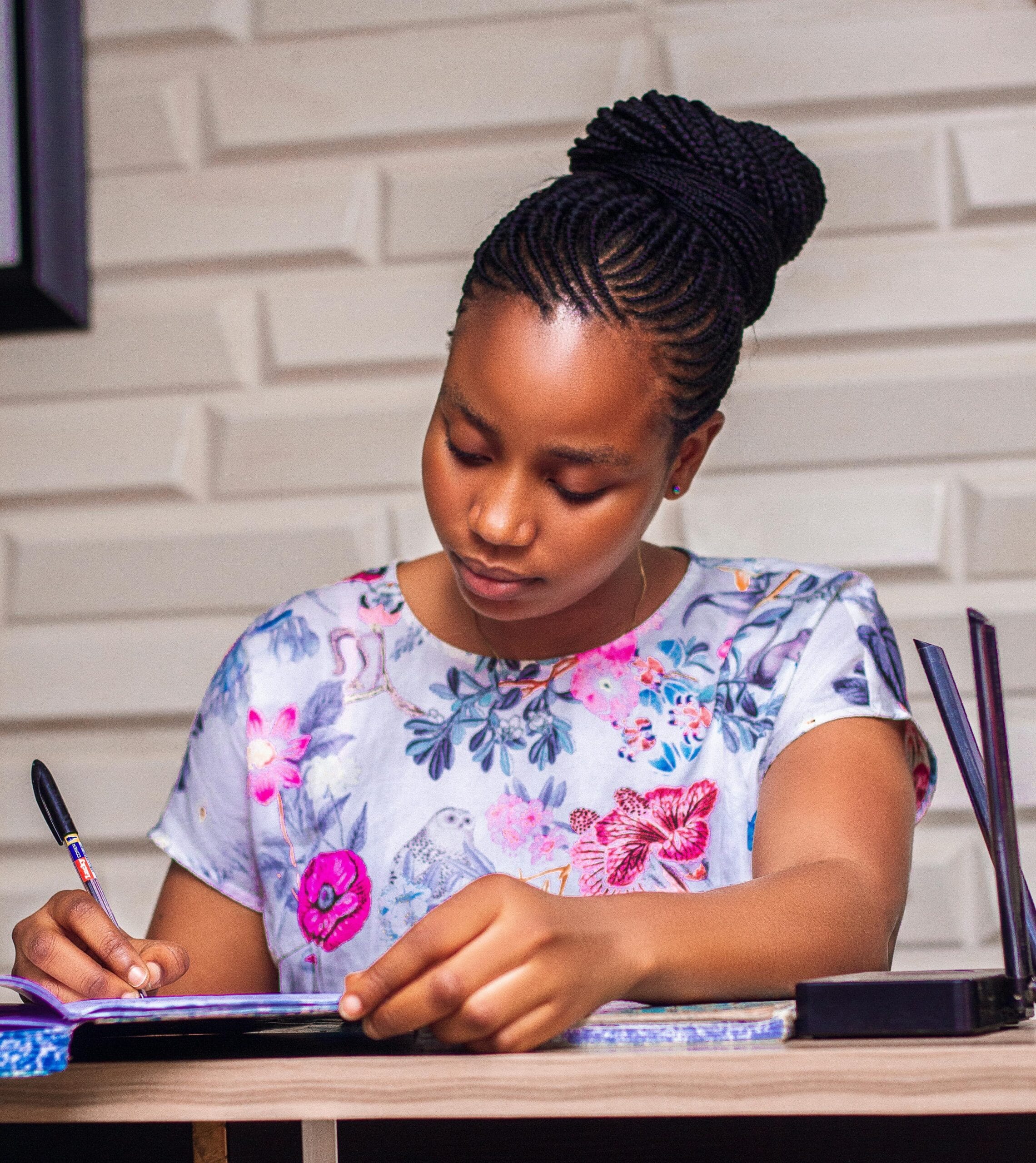 A young Nigerian female student sitting on a chair with a table and writing her note