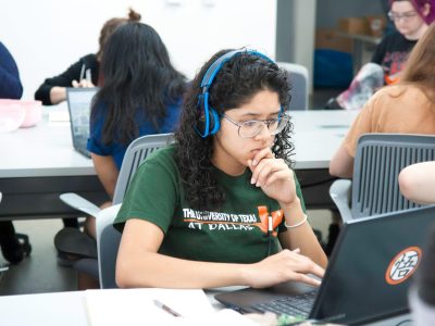 A female university student wearing blue headphones and studying on her Laptop